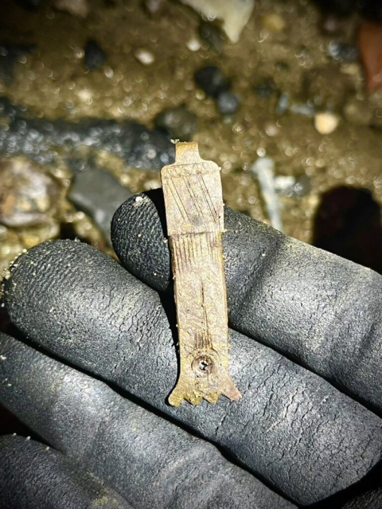 A decorated copper alloy book clasp held in a gloved hand on the Thames foreshore at night